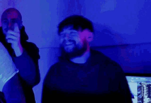 a man with a beard is standing in front of a computer in a room with blue lights .