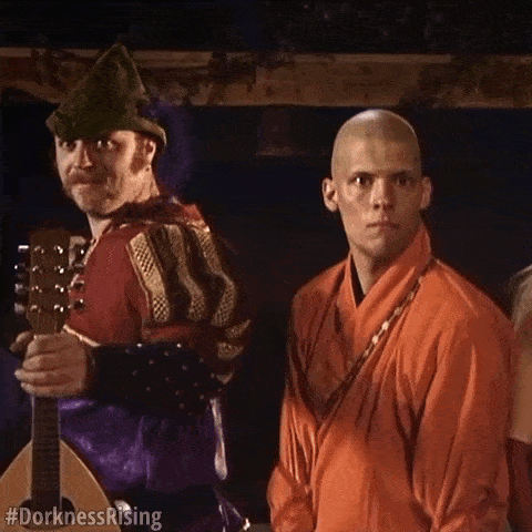 a man in a green hat is holding a guitar while standing next to a man in an orange robe .