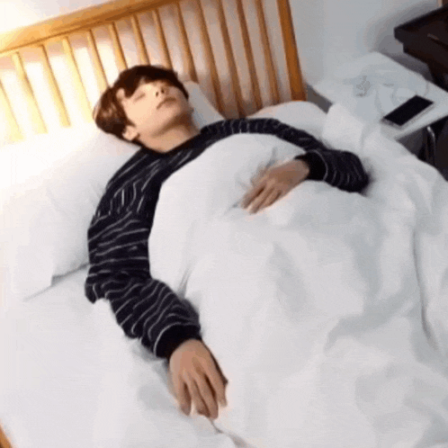 a young man is laying in a bed with a white blanket and a striped shirt on .