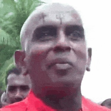 a man with a tattoo on his forehead is wearing a red shirt and looking at the camera .