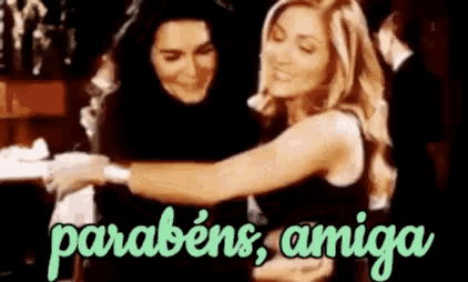 two women are hugging each other and the words parabéns amiga are on the bottom of the picture .