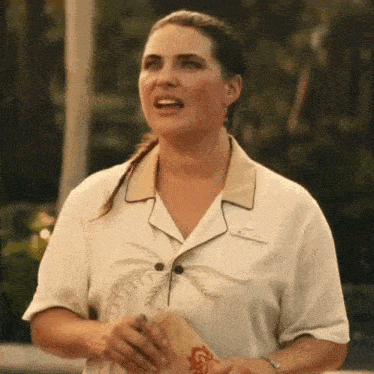 a woman wearing a white shirt with palm trees on it is standing in front of a pool .