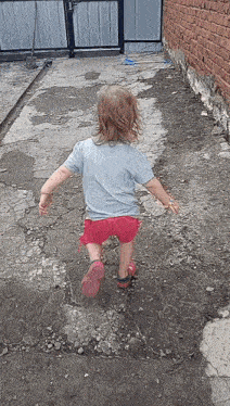 a little girl in a blue shirt and red shorts is running on a dirt path