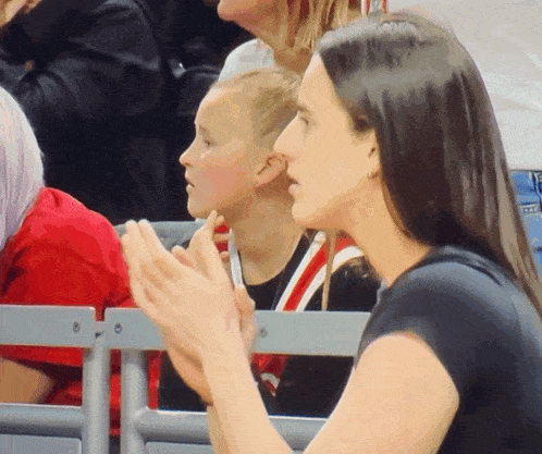 a woman in a black shirt sits in a stadium with a child