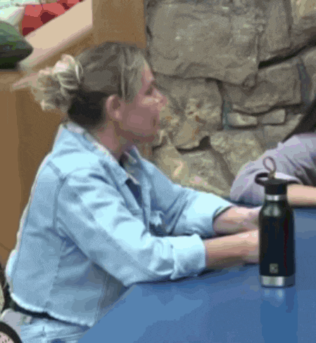 a woman in a denim shirt sits at a table with a water bottle on it