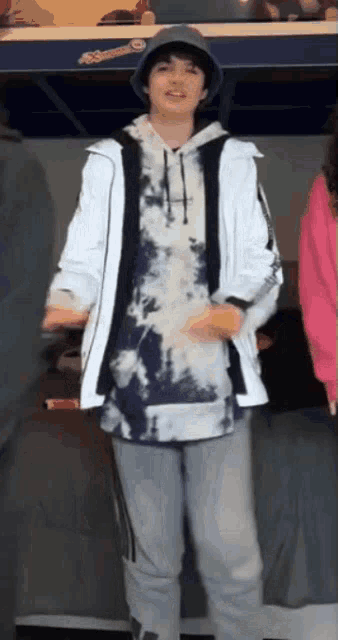 a young boy wearing a tie dye hoodie and a bucket hat is standing in a room .