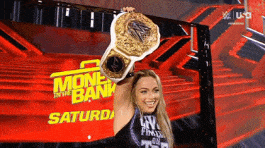 a woman is holding up a wrestling championship belt in front of a sign that says money in the bank