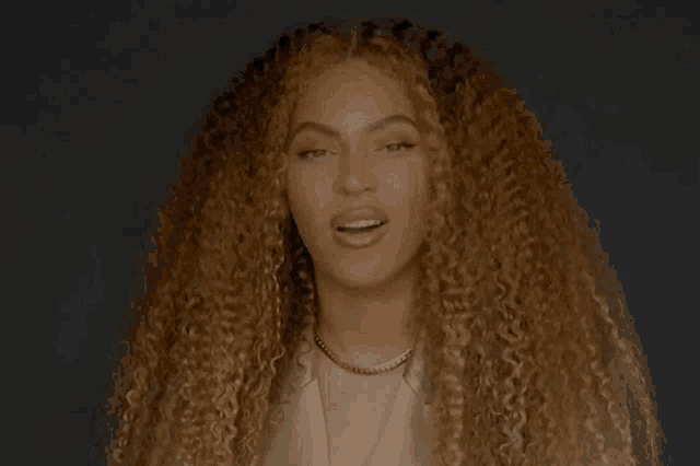 a woman with long curly hair is wearing a necklace