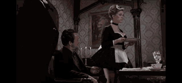 a woman in a maid 's outfit is serving food to a man in a tuxedo
