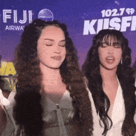two women standing in front of a sign that says 102.7 fiji airway