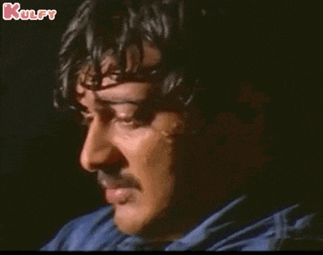 a man with a mustache is crying with his mouth open in a dark room .