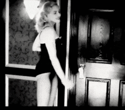 a black and white photo of a woman in a black dress standing in front of a door