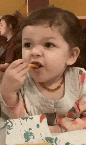 a little girl wearing a necklace is eating a snack