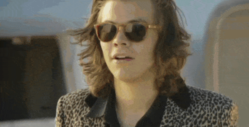 a man with long hair wearing sunglasses and a leopard print jacket .