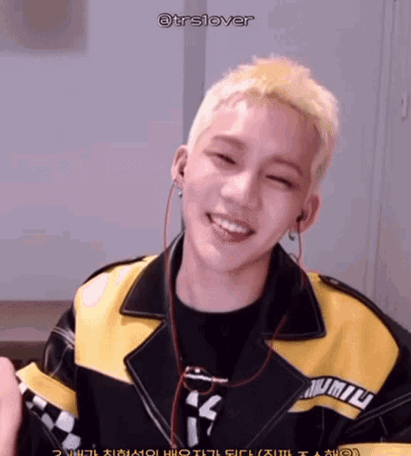 a young man wearing a yellow and black jacket and earphones is smiling .