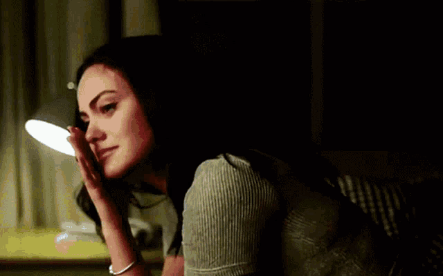 a woman is sitting in a dark room with her hand to her face