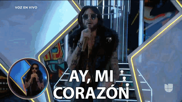 a man singing into a microphone with the words " ay mi corazon " behind him
