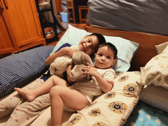 two young boys are laying on a bed and one is holding a teddy bear