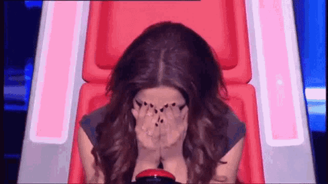 a woman is covering her face with her hands while sitting in a chair .