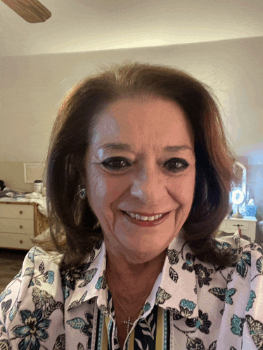 a woman wearing a floral shirt and a cross smiles for the camera