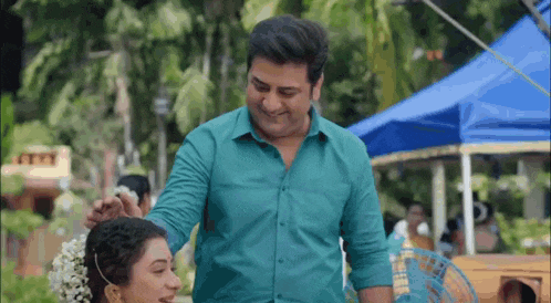 a man in a blue shirt is putting a flower in the hair of a woman .