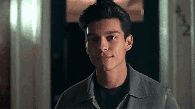 a young man in a gray shirt is standing in front of a door and smiling .