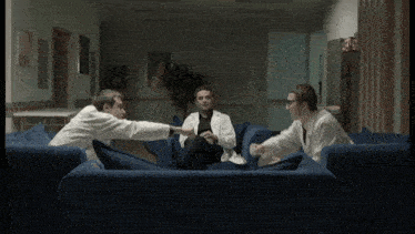 three men in lab coats are sitting on a blue couch and talking
