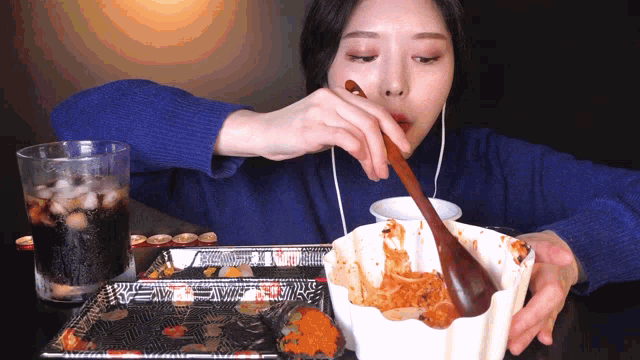 a woman in a blue sweater is eating a bowl of food