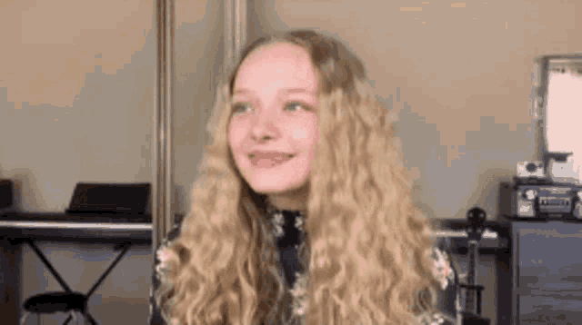 a young girl with long blonde hair is standing in front of a piano .