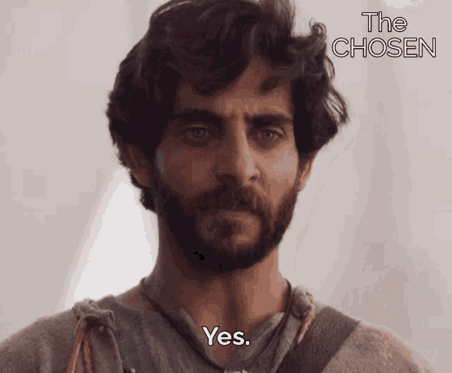 a man with a beard says yes in front of a sign that says " the chosen "