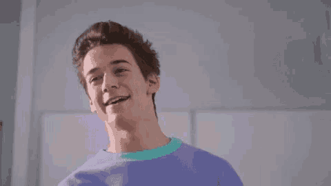 a young man wearing a purple sweater is smiling and looking at the camera .
