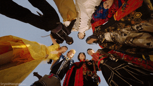 a group of people are standing in a circle with dryedmango.com written on the bottom right