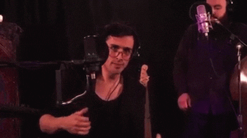 a man wearing headphones and glasses is giving a thumbs up sign in front of a microphone .