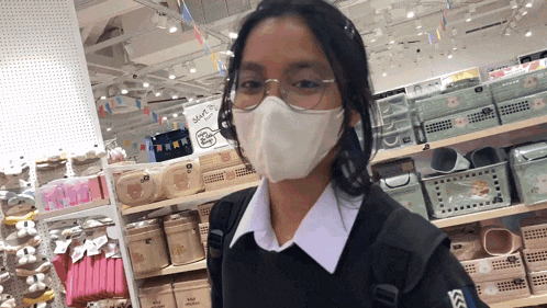 a girl wearing a mask and glasses stands in front of a shelf with baskets and boxes on it