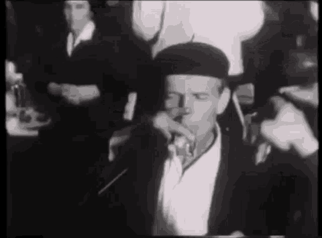 a man in a black hat is drinking from a glass in a crowd of people .