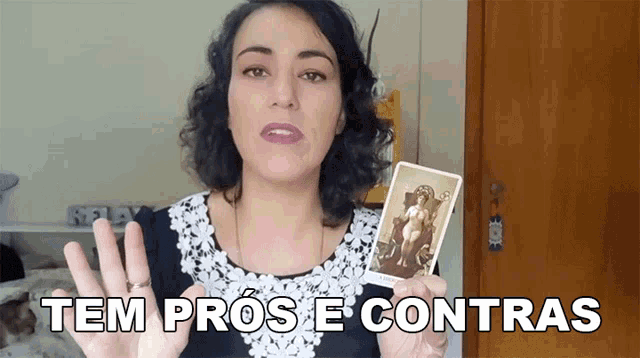 a woman holding up a tarot card with the words tem pros e contras written below her