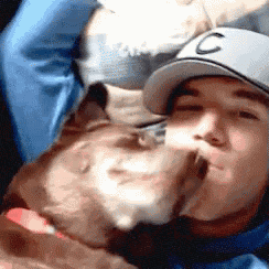 a man wearing a baseball cap with the letter c on it is kissing a dog
