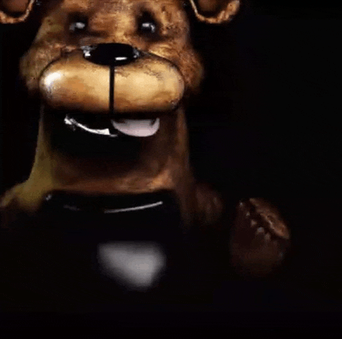 a close up of a teddy bear 's face in the dark with its tongue out .