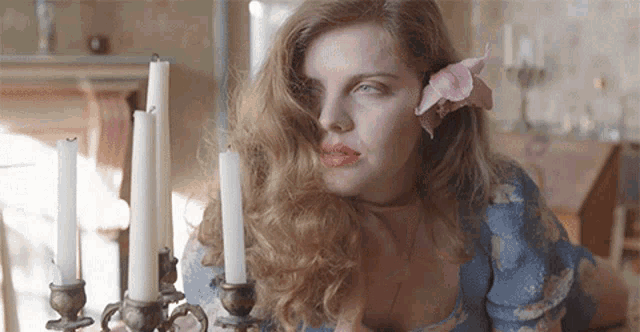 a woman with a pink flower in her hair is looking at candles