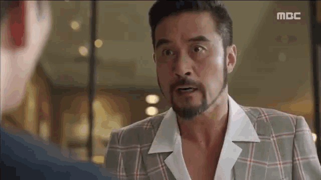 a man with a beard is wearing a plaid suit and white shirt .