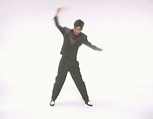 a man in a suit is dancing in front of a white wall