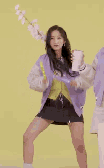 a woman in a purple jacket is holding a flower and a cup of coffee while dancing .