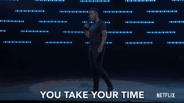 a man is standing on a stage holding a microphone and says you take your time .