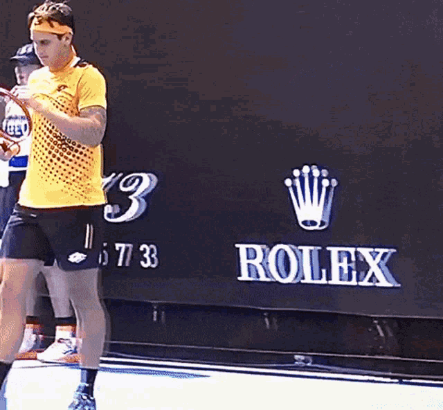 a man in a yellow shirt is holding a tennis racquet in front of a rolex sign