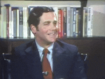 a man in a suit and tie is smiling in front of a book shelf