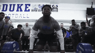a man lifting a barbell in front of a duke football sign