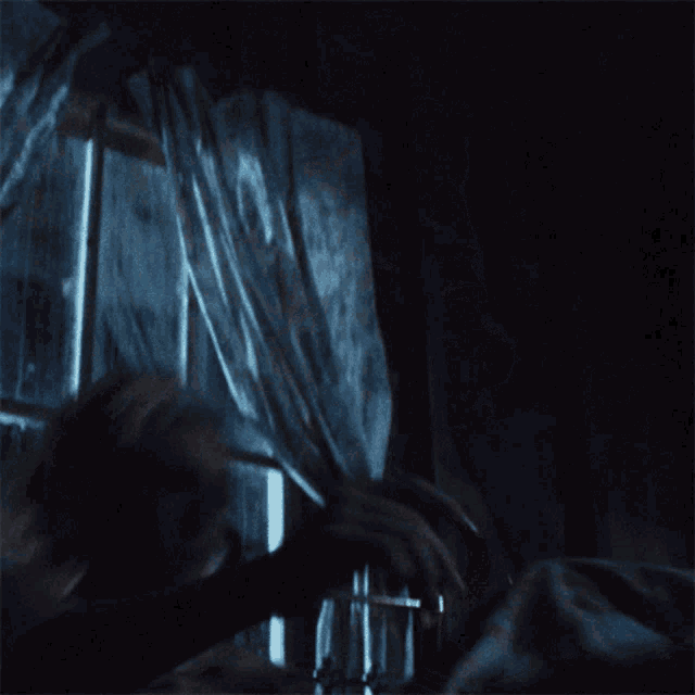 a woman in a white tank top looks out a window in the dark