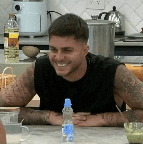 a man with tattoos sits at a table with a bottle of aquafina water in front of him
