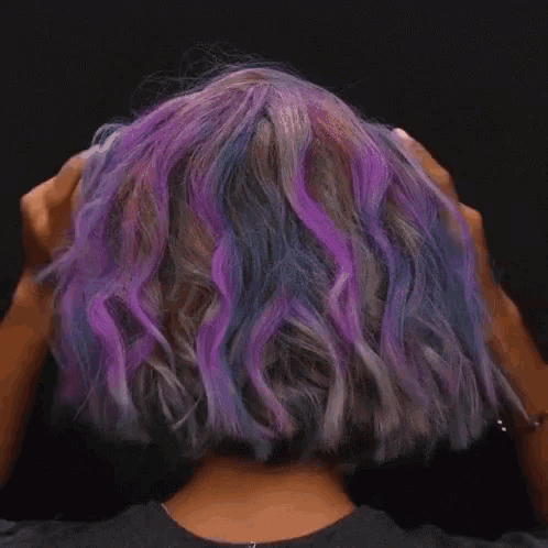 a woman with purple and blue hair is holding her hair with her hands