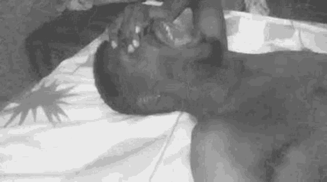 a black and white photo of a shirtless man laying on a bed with his eyes closed .